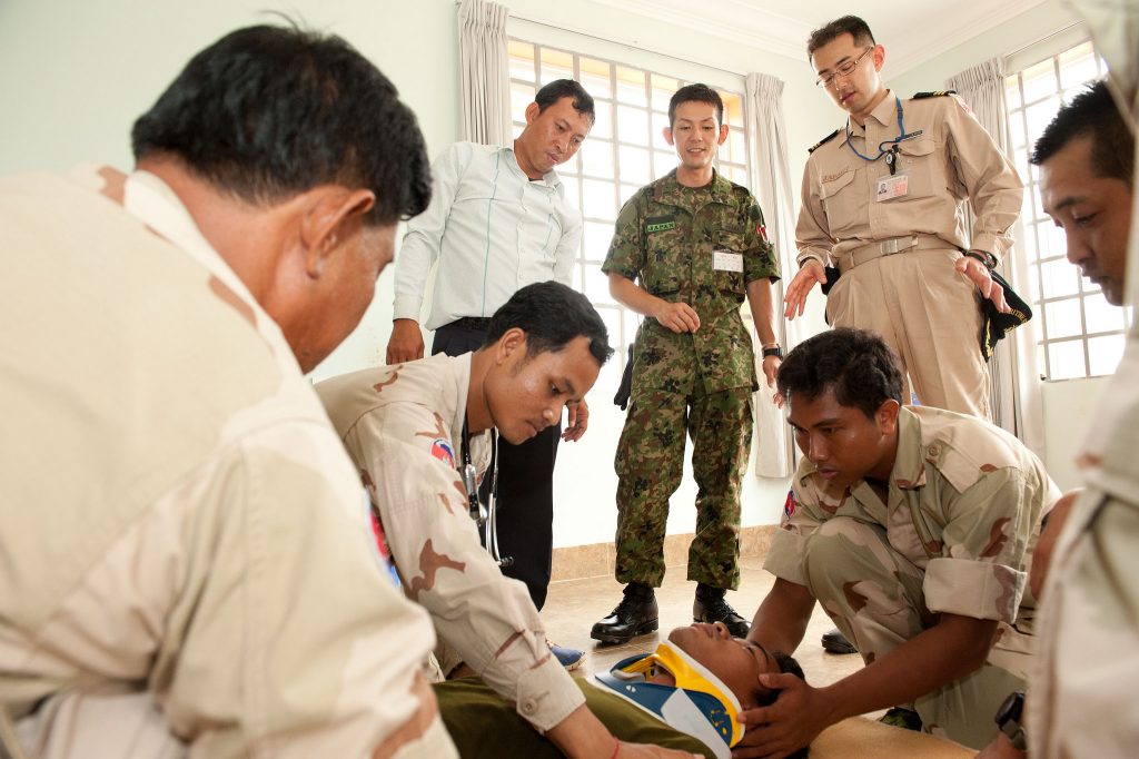 Japanese military members observe as Cambodian sailors attach a neck brace to a patient during a Pacific Partnership knowledge exchange in Sihanoukville, Cambodia.